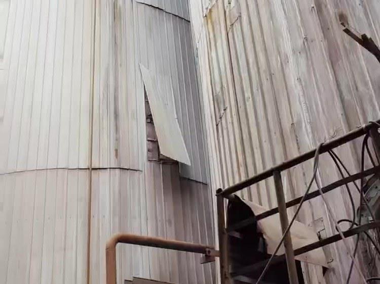 相邻两台槽体外壁：一块压型护板破损下垂，板缝位置锈迹连片